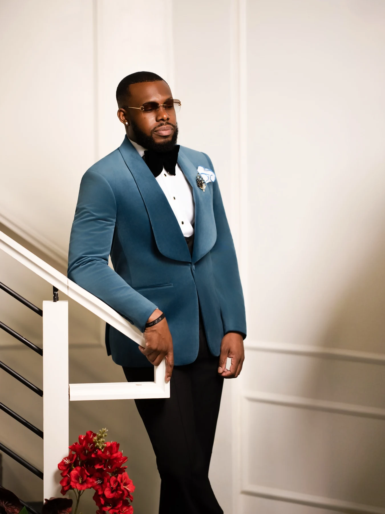 Full-length editorial portrait in a blue tuxedo beside a staircase