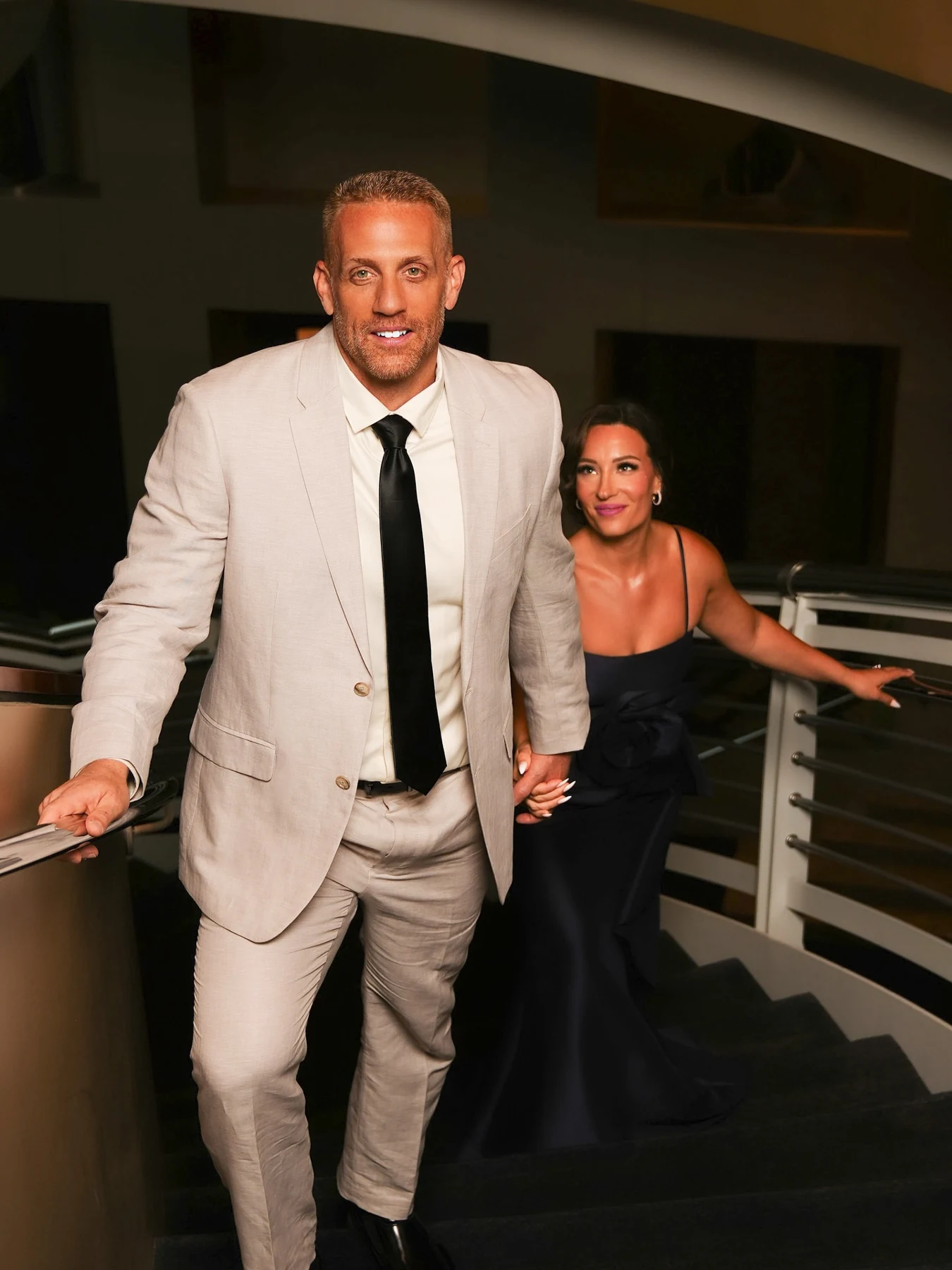 Couple holding hands on a staircase in a light suit and black gown