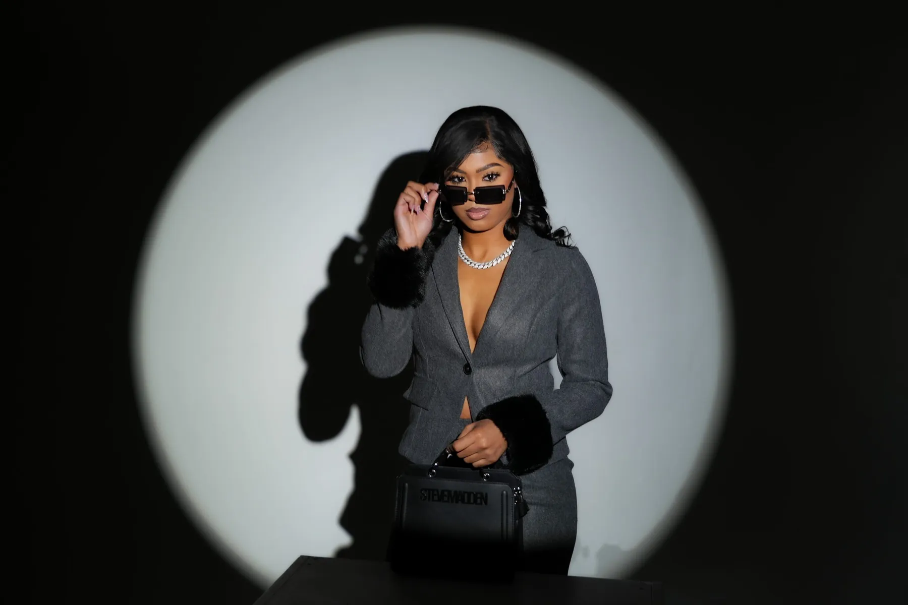 Portrait in a grey blazer and sunglasses within a circular studio spotlight